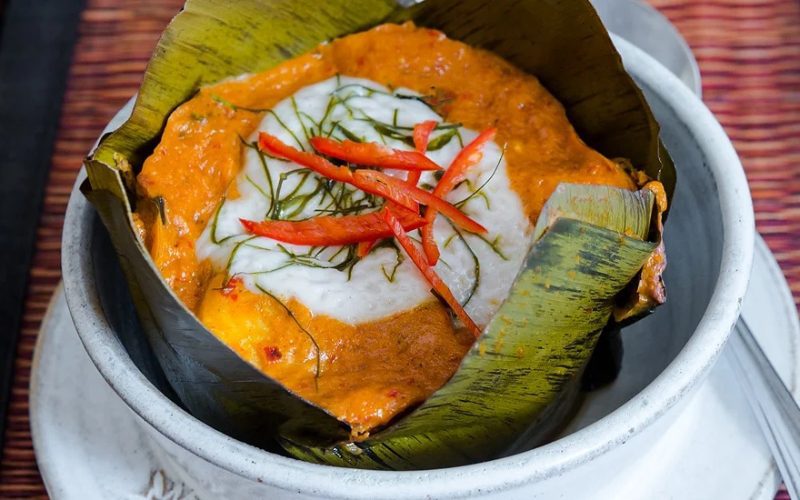 Amok de Poisson, présenté dans une feuille de bananier, avec une garniture de lait de coco, des zestes de citron kaffir et des lamelles de piment rouge
