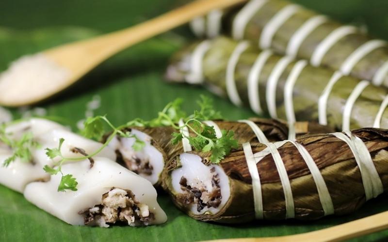 Plat traditionnel vietnamien bánh tẻ, gâteau de riz gluant enveloppé dans des feuilles vertes, présenté ici coupé en morceaux révélant une farce parfumée, décoré de coriandre fraîche