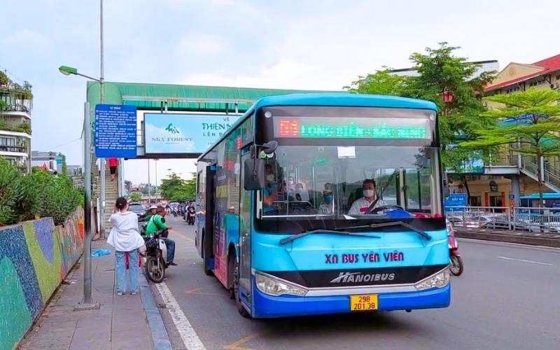 Bus bleu de la ligne Hanoi – Bac Giang à l’arrêt, avec des passagers à l’intérieur et des piétons ainsi que des motos circulant sur le trottoir voisin