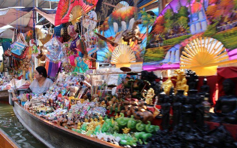 Une boutique de souvenirs flottante au marché de Damnoen Saduak, proposant des éventails colorés, des sculptures artisanales et divers objets traditionnels thaïlandais