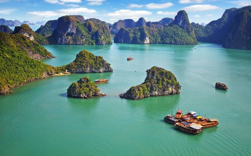Vue aérienne spectaculaire de la baie d’Halong au Vietnam, avec ses formations karstiques recouvertes de végétation et ses jonques traditionnelles naviguant sur les eaux vert émeraude