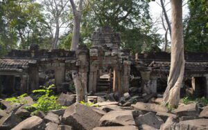 Ruines d’un ancien temple en pierre, partiellement effondré et envahi par la végétation, avec de grands arbres aux racines imposantes s’entremêlant aux structures