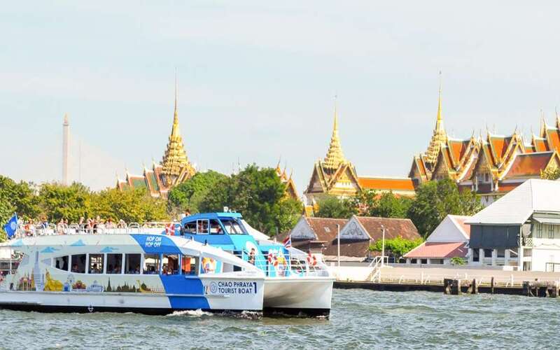 Bateau touristique Chao Phraya naviguant sur le fleuve à Bangkok, avec en arrière-plan les toits dorés du Grand Palais et des temples thaïlandais