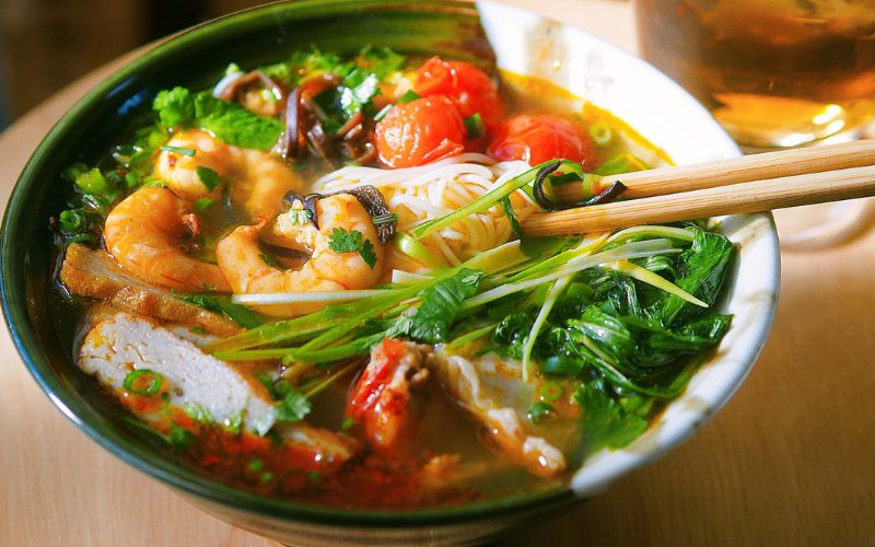 Bol de soupe de nouilles aux crevettes (bún tôm) garnie de légumes frais, tomates, champignons et herbes aromatiques, plat typique de l’île de Cat Ba