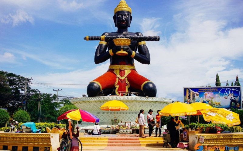 Statue géante de Ta Dambong à Battambang, Cambodge, avec des visiteurs et des stands colorés de parasols au premier plan