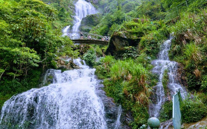Cascade Thác Bạc à Sapa, dévalant en plusieurs niveaux au cœur d’une végétation luxuriante, avec un pont en bois permettant aux visiteurs d’admirer de près la beauté naturelle du site