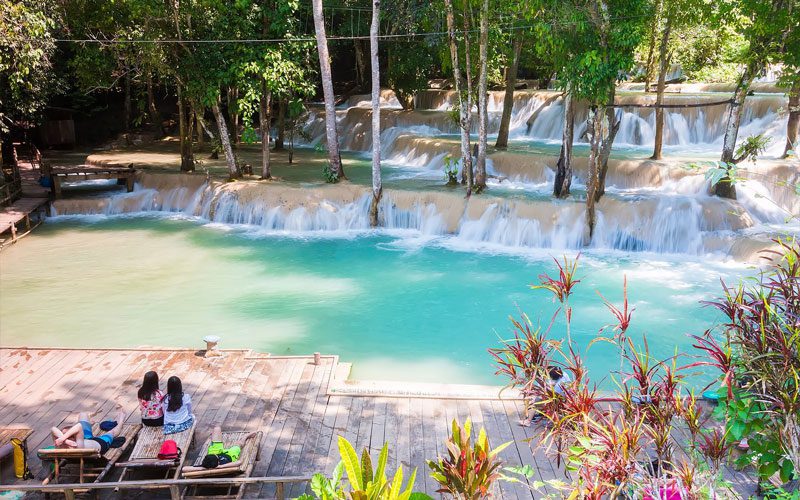 Cascade de Tad Sae, avec ses bassins turquoise en terrasse entourés de forêt tropicale et des visiteurs se relaxant sur une plateforme en bois