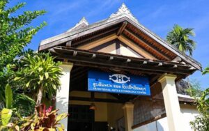 Façade du Centre des Arts Traditionnels et d'Ethnologie à Luang Prabang, entourée de verdure, avec son enseigne bleue caractéristique