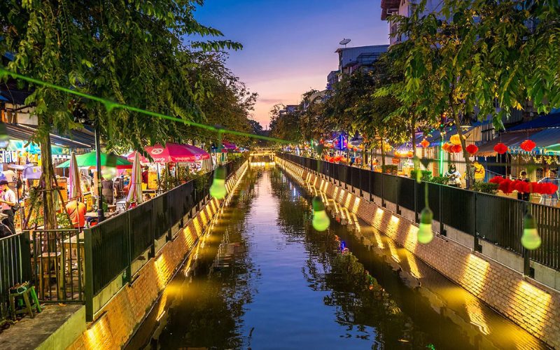 Vue du canal Ong Ang à Bangkok en soirée, bordé de stands de street food, de guirlandes lumineuses et de lanternes rouges