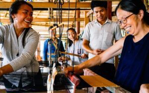 Atelier de tissage traditionnel, avec des artisans locaux souriants partageant leur savoir-faire dans une ambiance conviviale et chaleureuse