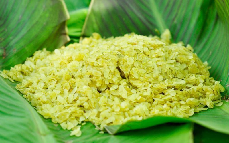 Gros plan sur une portion de cốm, flocons de riz gluant jeunes de couleur vert clair, délicatement disposés sur une feuille de bananier fraîche