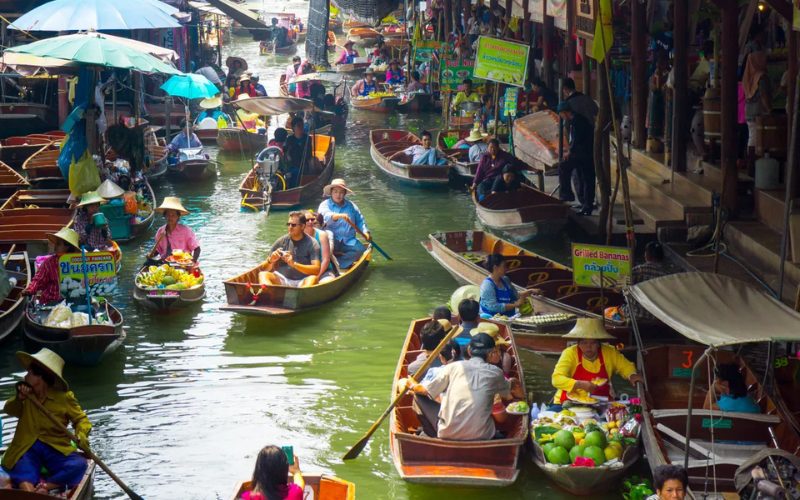 Scène animée du marché flottant de Damnoen Saduak en Thaïlande, où des vendeurs en barques traditionnelles proposent des fruits, légumes et plats locaux