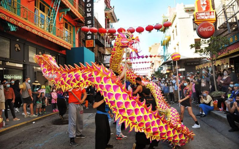 Danse du dragon coloré dans une rue animée décorée de lanternes rouges lors d’un festival chinois, avec une foule de spectateurs portant des masques