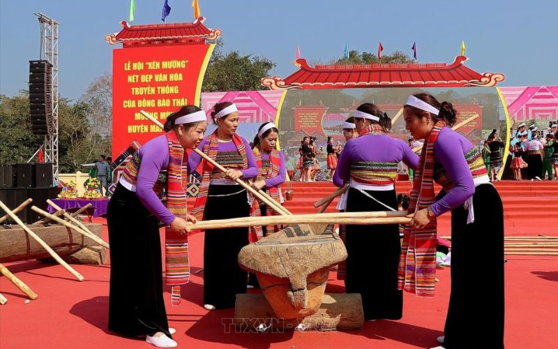 Femmes thaï en costumes traditionnels participant à la fête de Mai Chau, jouant du xên muong avec des maillets en bois lors d’une performance culturelle colorée
