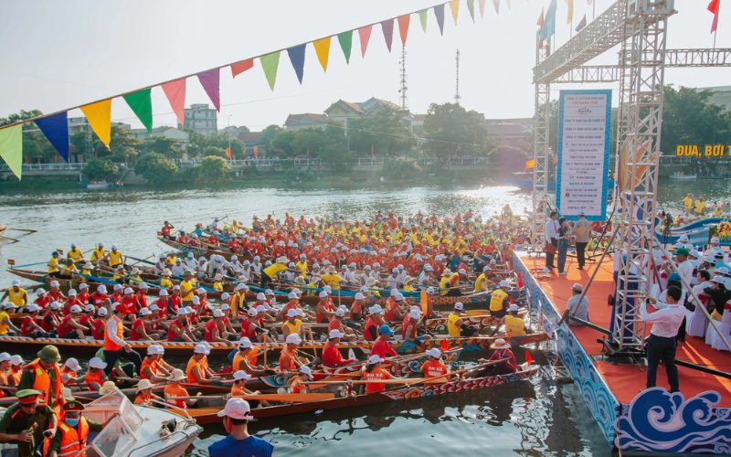 Des centaines de rameurs en tenue colorée se préparent pour une course de bateaux traditionnels sur une rivière lors du Festival des Bateaux de Course à Hội An