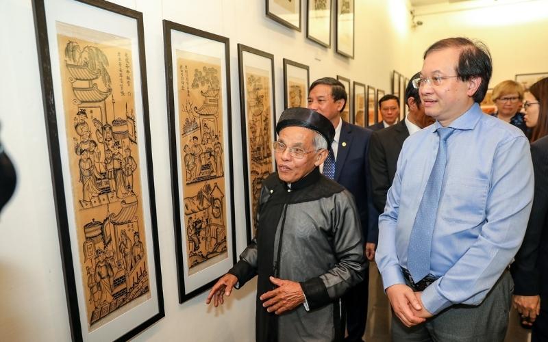 Exposition d’estampes traditionnelles de Đông Hồ à Bắc Ninh, avec des visiteurs et un maître artisan présentant les œuvres encadrées accrochées aux murs de la galerie