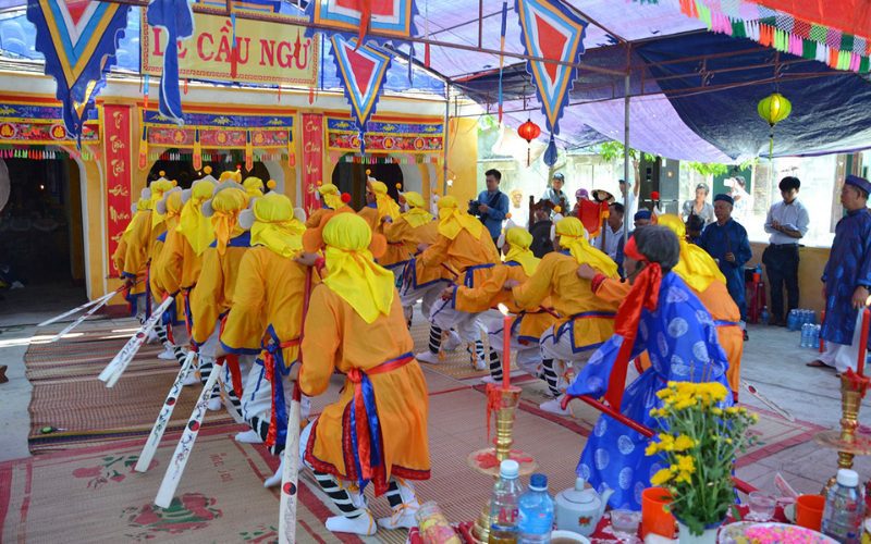 Cérémonie traditionnelle du festival Cầu Ngư au Vietnam, avec des participants vêtus de costumes colorés jaune, bleu et rouge