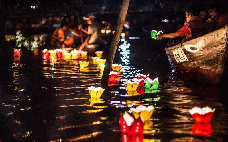 Des lanternes flottantes colorées illuminant la rivière de Hoi An lors du Festival des lanternes, tandis que des habitants et touristes participent à cette tradition spirituelle
