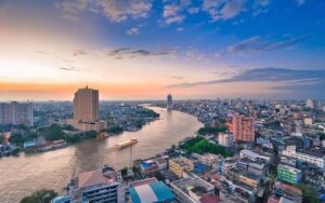 Vue aérienne du fleuve Chao Phraya à Bangkok au coucher du soleil, entouré de gratte-ciels, de bâtiments et d'une ville animée sous un ciel coloré