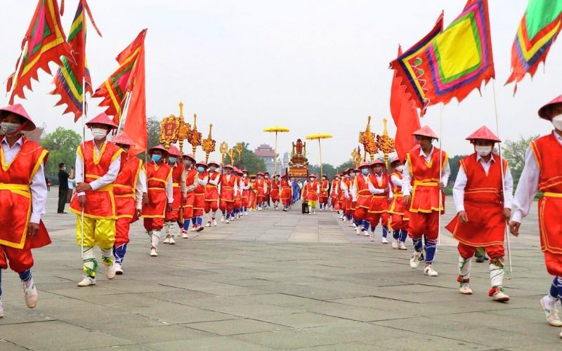 Procession traditionnelle lors de la fête des rois Hung à Phu Tho, avec des participants en costume rouge portant des drapeaux colorés et des palanquins cérémoniels