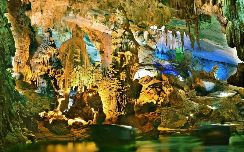 Intérieur spectaculaire de la grotte de Phong Nha, avec stalactites et stalagmites illuminées de lumières colorées se reflétant sur l’eau