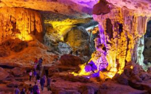 Intérieur de la grotte Sửng Sốt dans la baie d’Halong, Vietnam, illuminé par des lumières colorées mettant en valeur les formations spectaculaires de stalactites et stalagmites, avec des visiteurs explorant le site sur un chemin aménagé