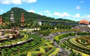 Vue panoramique du jardin tropical de Nong Nooch, avec ses aménagements paysagers impressionnants, ses statues et ses pavillons traditionnels sous un ciel bleu éclatant
