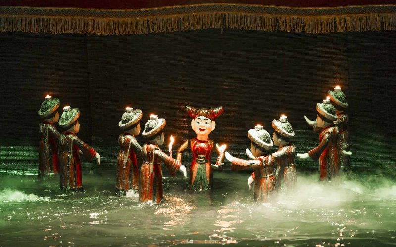 Spectacle de marionnettes sur l’eau au Vietnam, avec des figurines traditionnelles richement colorées évoluant à la surface de l’eau, éclairées par des bougies et des effets de lumière