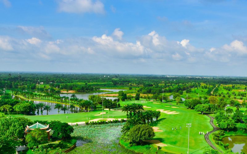 Vue aérienne d’un vaste parcours de golf luxuriant avec des fairways impeccables, des bunkers bien dessinés, des plans d’eau et des palmiers