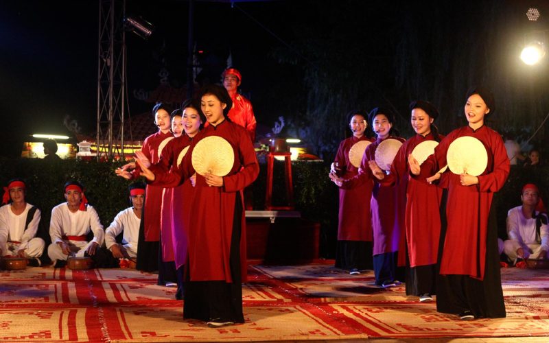 Spectacle de chant xoan à Phu Tho, avec des artistes en áo dài rouges tenant des éventails ronds, accompagné de musiciens traditionnels