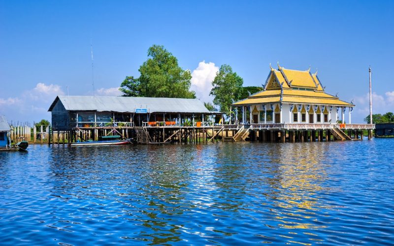 Temple bouddhiste et maison sur pilotis au bord du Tonlé Sap, le plus grand lac du Cambodge, sous un ciel bleu éclatant