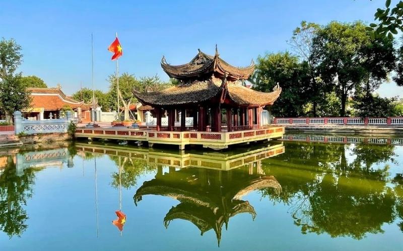 Maison communale de Tam Tảo à Bắc Ninh, pavillon traditionnel en bois au toit recourbé situé au milieu d’un étang, reflété dans l’eau calme et entouré de verdure