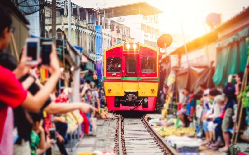 Train traversant le marché ferroviaire de Maeklong en Thaïlande, entouré de vendeurs et de touristes prenant des photos dans une atmosphère animée
