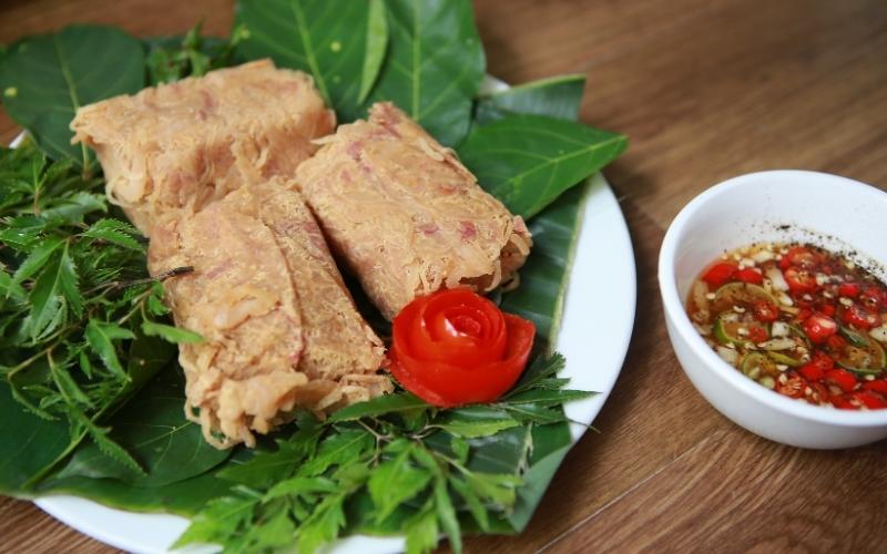 Plat traditionnel de nem chua vietnamien, présenté sur des feuilles vertes avec herbes aromatiques et une rose en tomate, accompagné d’une sauce pimentée à l’ail et au vinaigre dans un petit bol