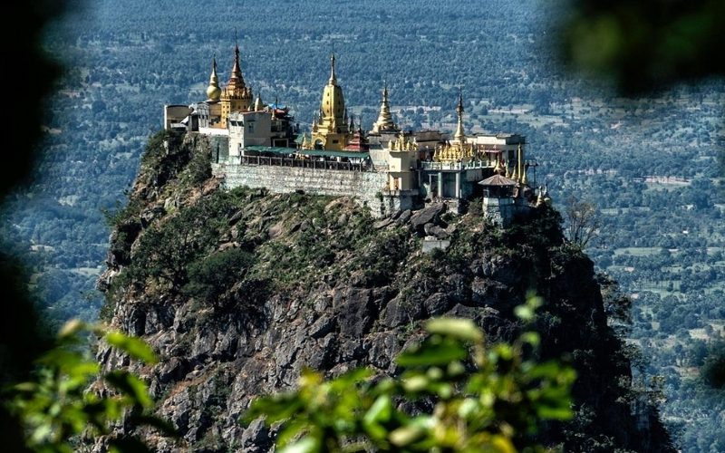 Vue panoramique d’un temple bouddhiste perché au sommet d’un piton rocheux, entouré de forêts et dominant une vaste plaine verdoyante au Myanmar