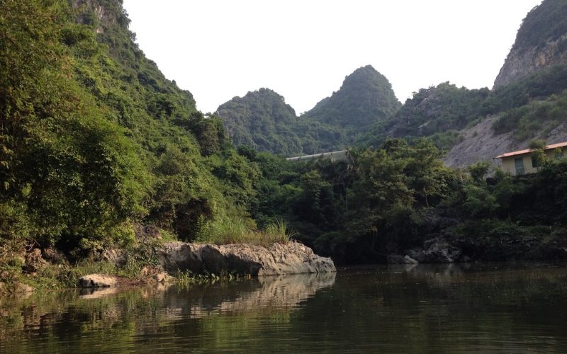 Paysage naturel de Hà Nam avec des montagnes calcaires couvertes de végétation dense, reflétées dans une rivière paisible bordée de rochers