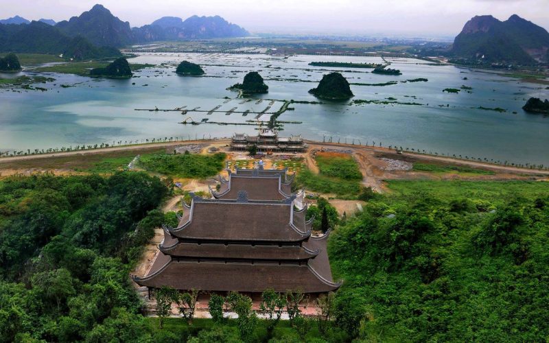 Vue panoramique du complexe bouddhiste de Tam Chúc à Hà Nam, avec son imposante pagode traditionnelle entourée de collines verdoyantes, face à un vaste lac parsemé d’îlots calcaires
