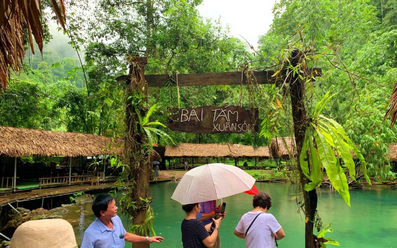 Zone de baignade naturelle de Xuân Sơn à Phu Tho, entourée de forêts verdoyantes, avec des visiteurs se promenant au bord de l’eau turquoise