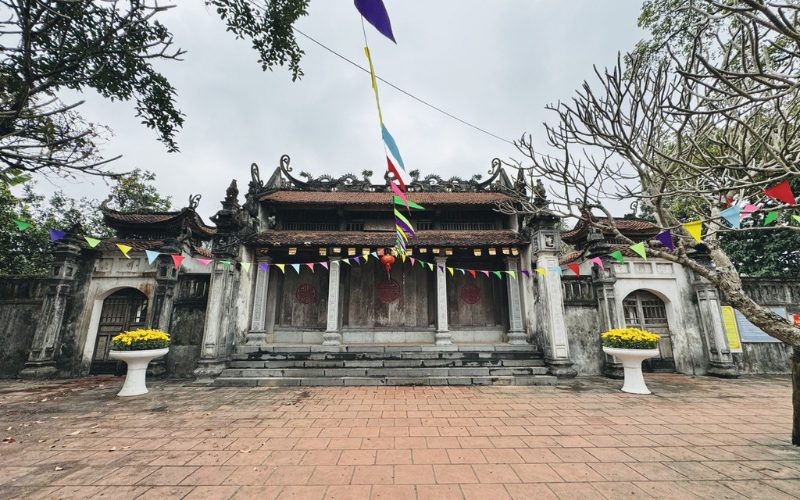 Ancienne pagode du village de Co Le à Nam Dinh, avec son toit de tuiles traditionnelles, ses portes sculptées et des fanions colorés suspendus pour une fête locale