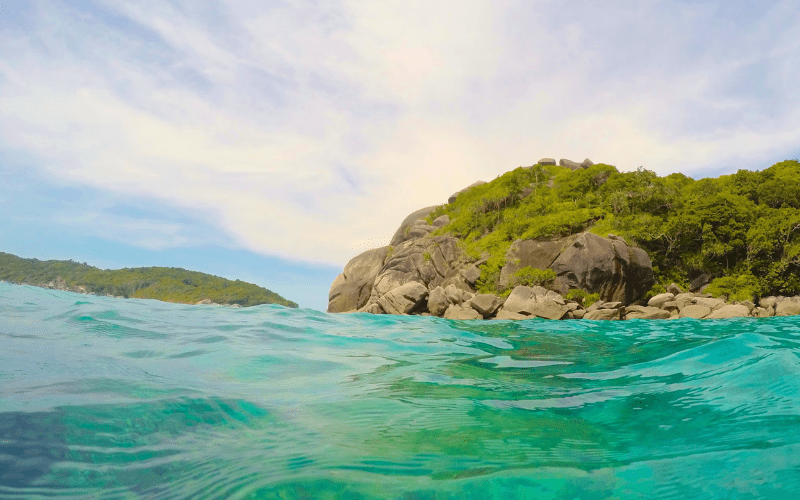 Une vue pittoresque d'une zone côtière avec une eau turquoise claire au premier plan et une colline rocheuse et boisée en arrière-plan