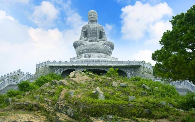 Grande statue en pierre de Bouddha assis en méditation à la pagode de Phật Tích, Bắc Ninh, érigée sur une colline verdoyante avec un ciel bleu en arrière-plan