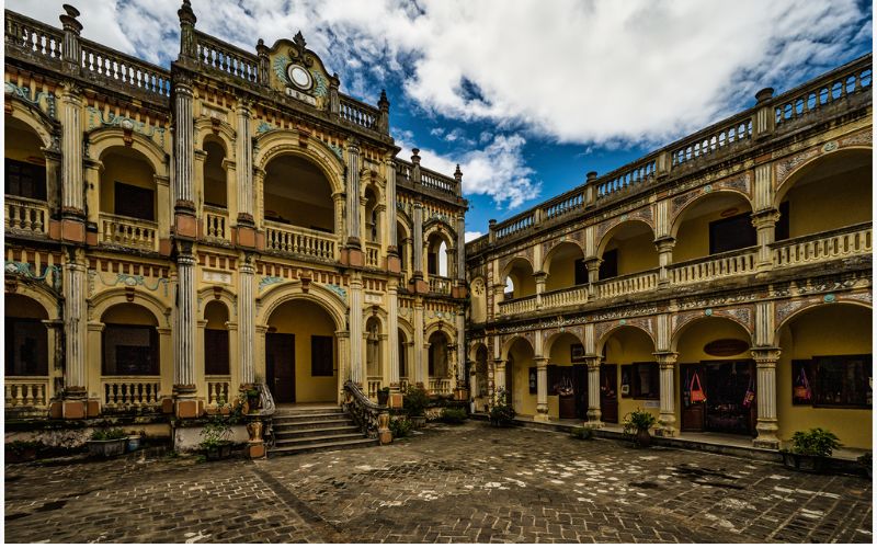 Cour intérieure du palais de la famille H’Mông à Sapa, imposant édifice de style architectural chinois et européen mêlés, avec ses arches élégantes, colonnes sculptées et façades richement décorées sous un ciel partiellement nuageux