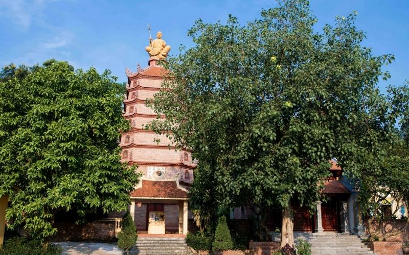 Tour de la pagode Dâu à Bắc Ninh, construite en briques avec plusieurs étages superposés, surmontée d’une statue dorée de Bouddha, entourée d’arbres verdoyants