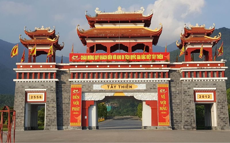 Porte monumentale du site spirituel de Tây Thiên au Vietnam, décorée de bannières rouges et de toits traditionnels ornés, avec les montagnes en arrière-plan
