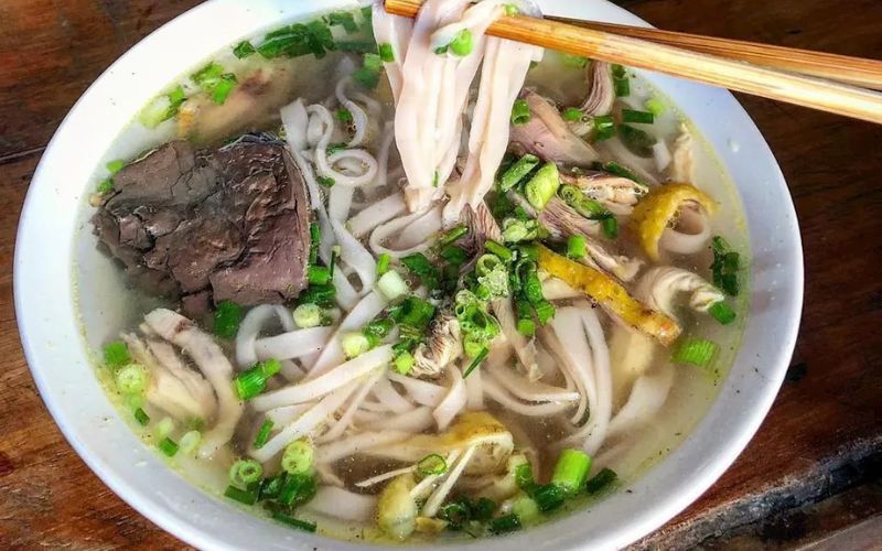 Bol fumant de phở gà de Sapa, composé de nouilles de riz, morceaux de poulet, herbes fraîches et ciboulette, servi dans un bouillon clair et parfumé