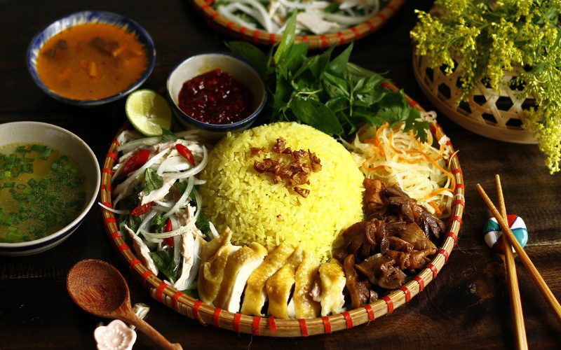 Assiette traditionnelle de Cơm Gà Hội An, avec du riz jaune parfumé, du poulet effiloché, des abats cuisinés, une salade d'herbes fraîches et d’oignons