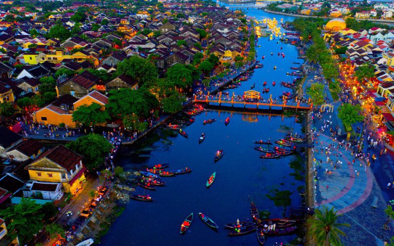 Vue aérienne nocturne de la vieille ville de Hoi An, avec la rivière animée de bateaux traditionnels et les maisons illuminées autour du pont