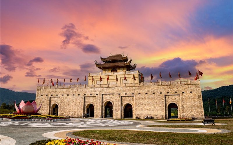 Complexe culturel et spirituel de Tây Yên Tử à Bắc Giang, avec son imposante porte et bâtiment de style impérial en pierre, sur fond de coucher de soleil aux couleurs flamboyantes