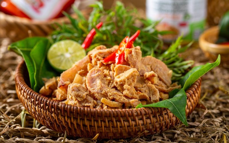 Plat traditionnel de thịt chua de Thanh Son à Phu Tho, porc fermenté assaisonné de son de riz grillé et de piment, servi dans un panier en bambou avec feuilles vertes et citron vert