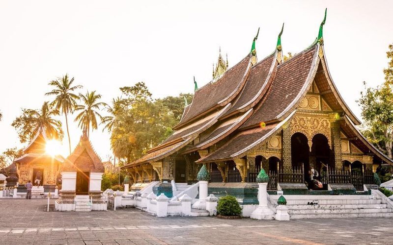 Temple Wat Xieng Thong à Luang Prabang, avec ses toits élégants descendant presque jusqu'au sol, baigné par la lumière du soleil couchant